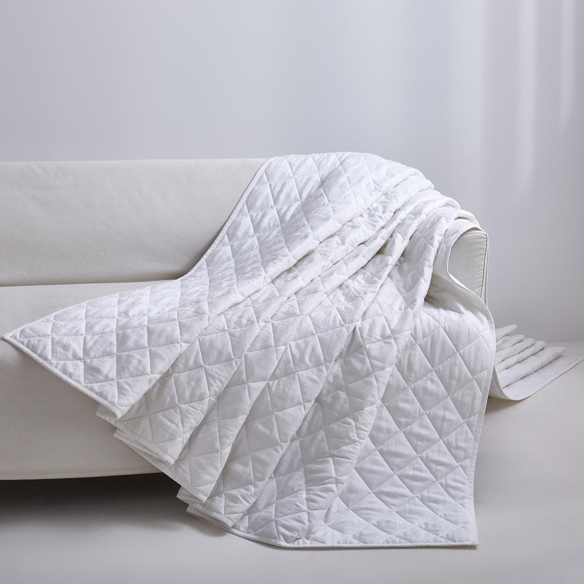 White Timeless Heritage Woven Quilt Set White blanket draped over a white sofa against a light gray background