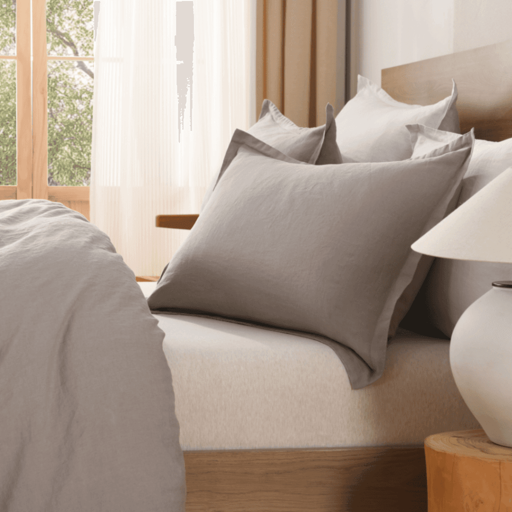 Neatly made bed with gray pillows and a lamp on a nightstand in a bedroom.