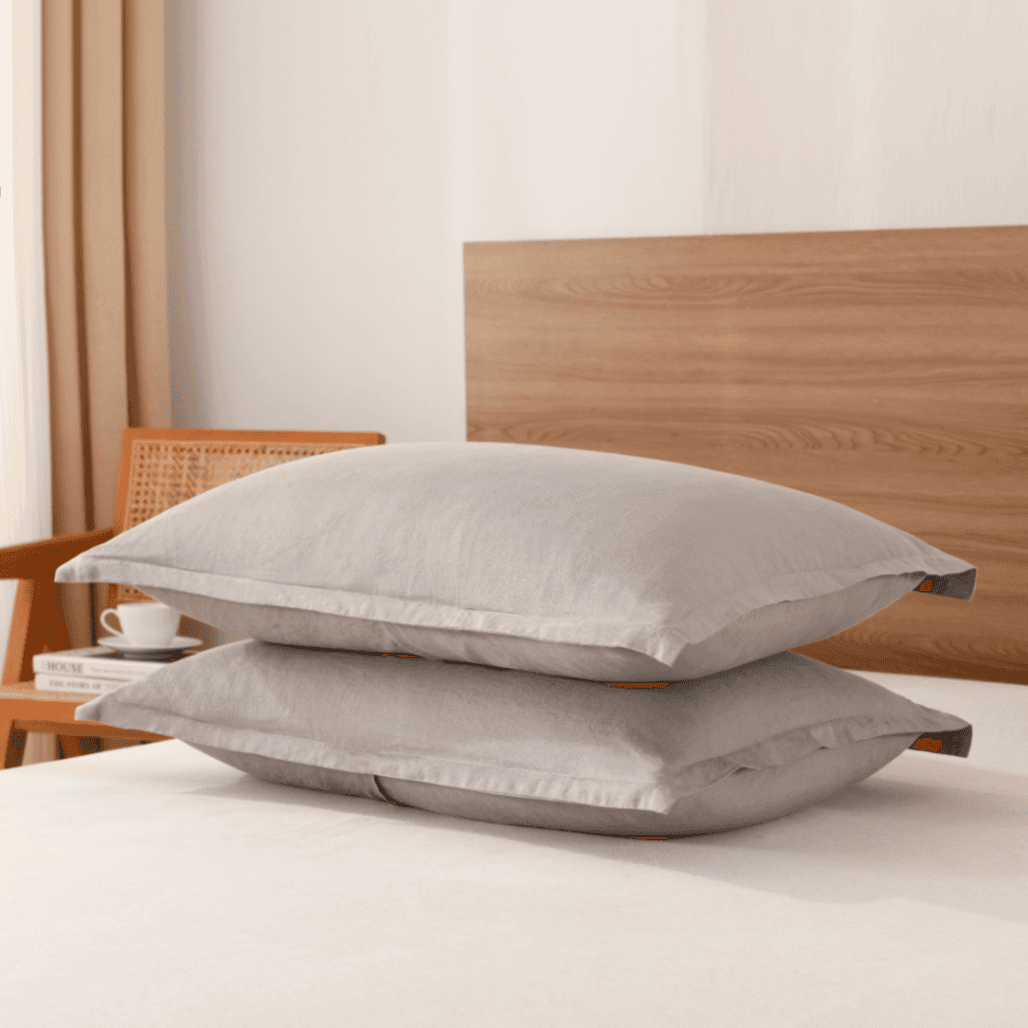 Two gray pillows stacked on a bed with a wooden headboard.