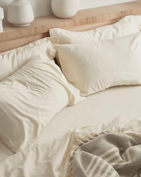 Neatly made bed with beige Organic Cotton 500 Thread Count Luxuriously Soft Sheet Set and pillows on a wooden headboard.