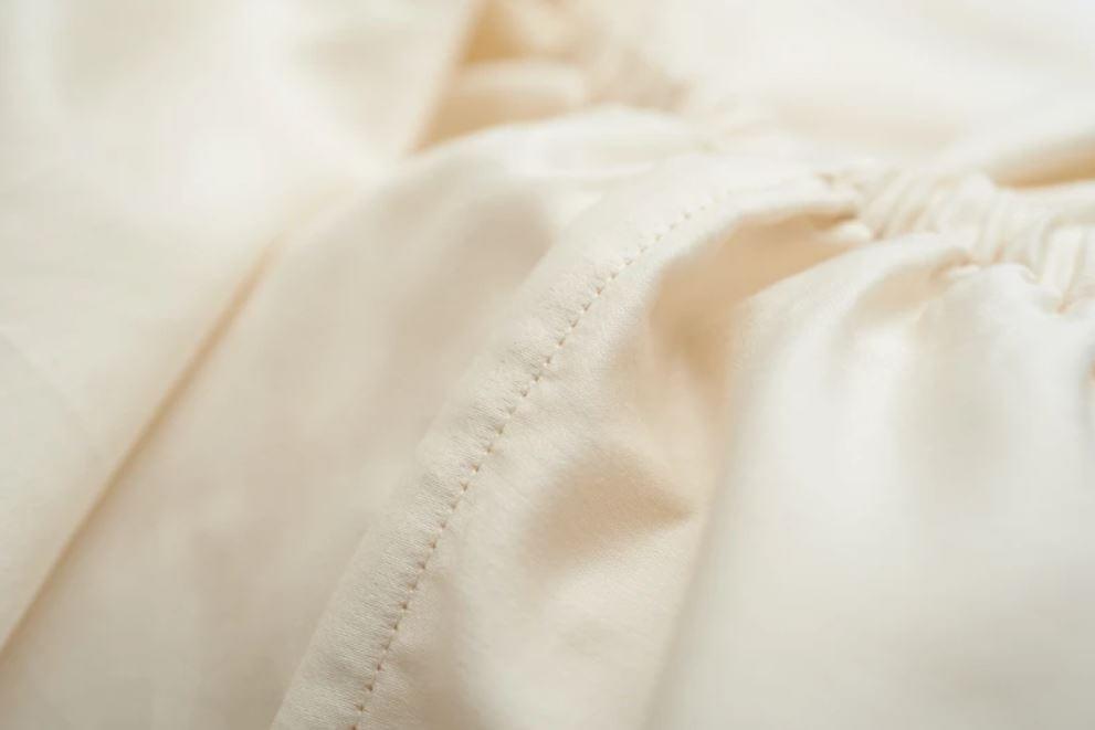 Close-up of beige Organic Cotton 500 Thread Count Luxuriously Soft Sheet Set with a focus on texture and stitching.