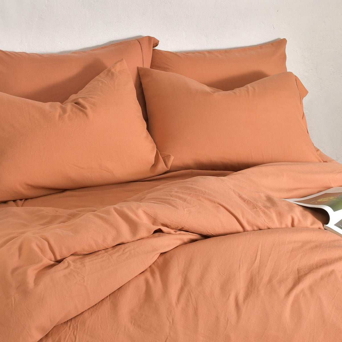 Orange bedding set with Bamboo Linen Pillowcase Pairs on a bed against a white wall.