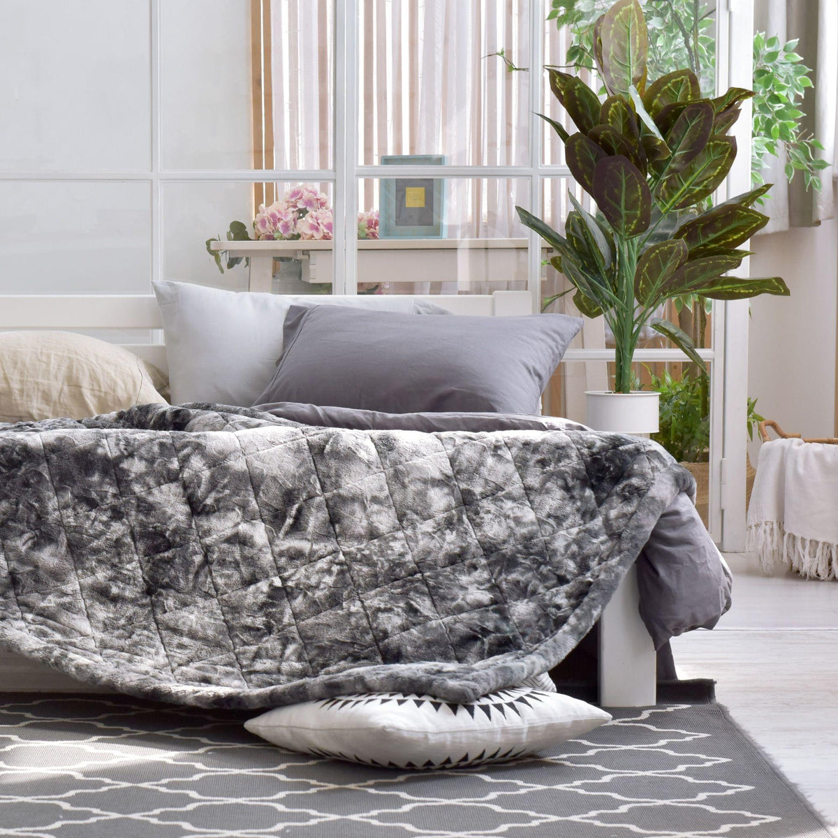 Hug Me Faux Weighted Throw Blanket on a bed in a bright bedroom with plants and decor.