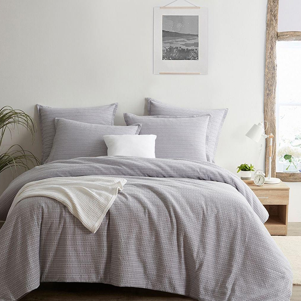 Gray checkered Seersucker Euro Sham set on a bed in a bright bedroom with a plant and framed picture.