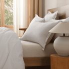Neatly made bed with pillows and a lamp on a nightstand in a bedroom.
