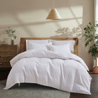 White Aurora Bloom Leaf Jacquard Duvet Cover Set White on a bed in a bedroom with plants and a lamp.