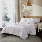 White Aurora Bloom Leaf Jacquard Quilt Set White on a bed in a bedroom with natural light
