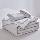 Stack of folded light gray comforters on a white surface