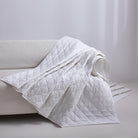 White Aurora Bloom Leaf Jacquard Quilt Set White draped over a gray sofa against a light gray background