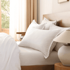 Neatly made bed with white pillows and a lamp on a nightstand in a well-lit bedroom.