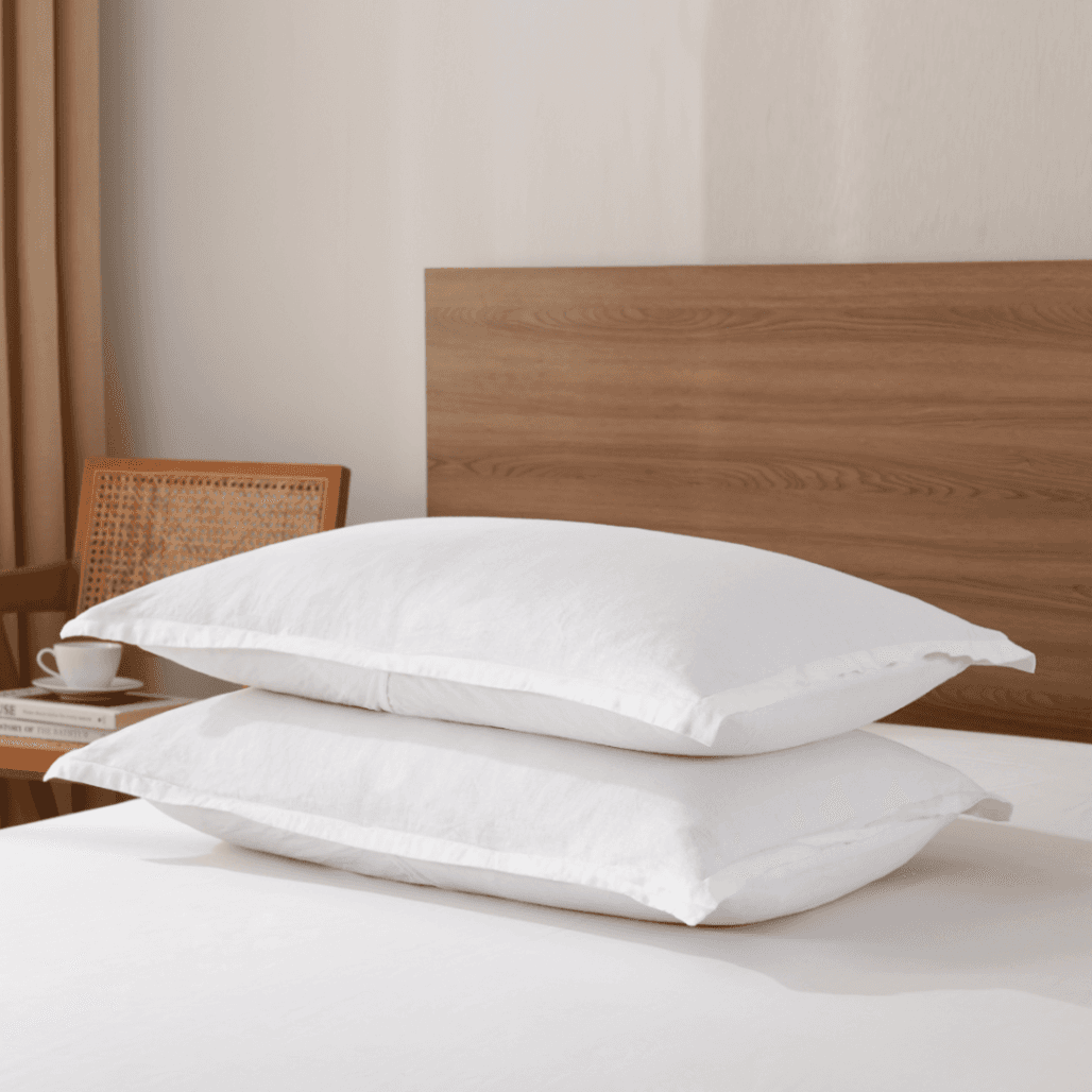 Two white pillows on a bed with a wooden headboard and a side table in the background.