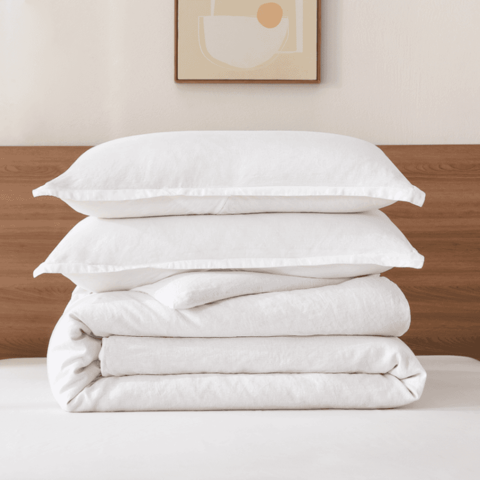 Stack of white pillows and duvet on a bed with a wooden headboard and abstract art in the background.