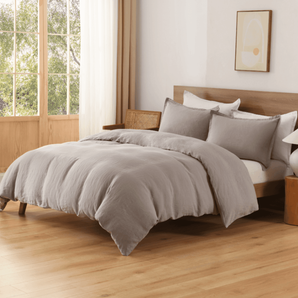 Gray comforter set on a bed in a bright bedroom with large windows.