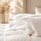 A neatly folded white All Season Bamboo Duvet White Insert item, likely a duvet cover or comforter, displayed on a bed in a softly lit bedroom setting with warm sunlight and blurred background decor.