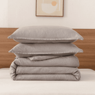 Stack of gray bedding on a bed with a wooden headboard and abstract art in the background.