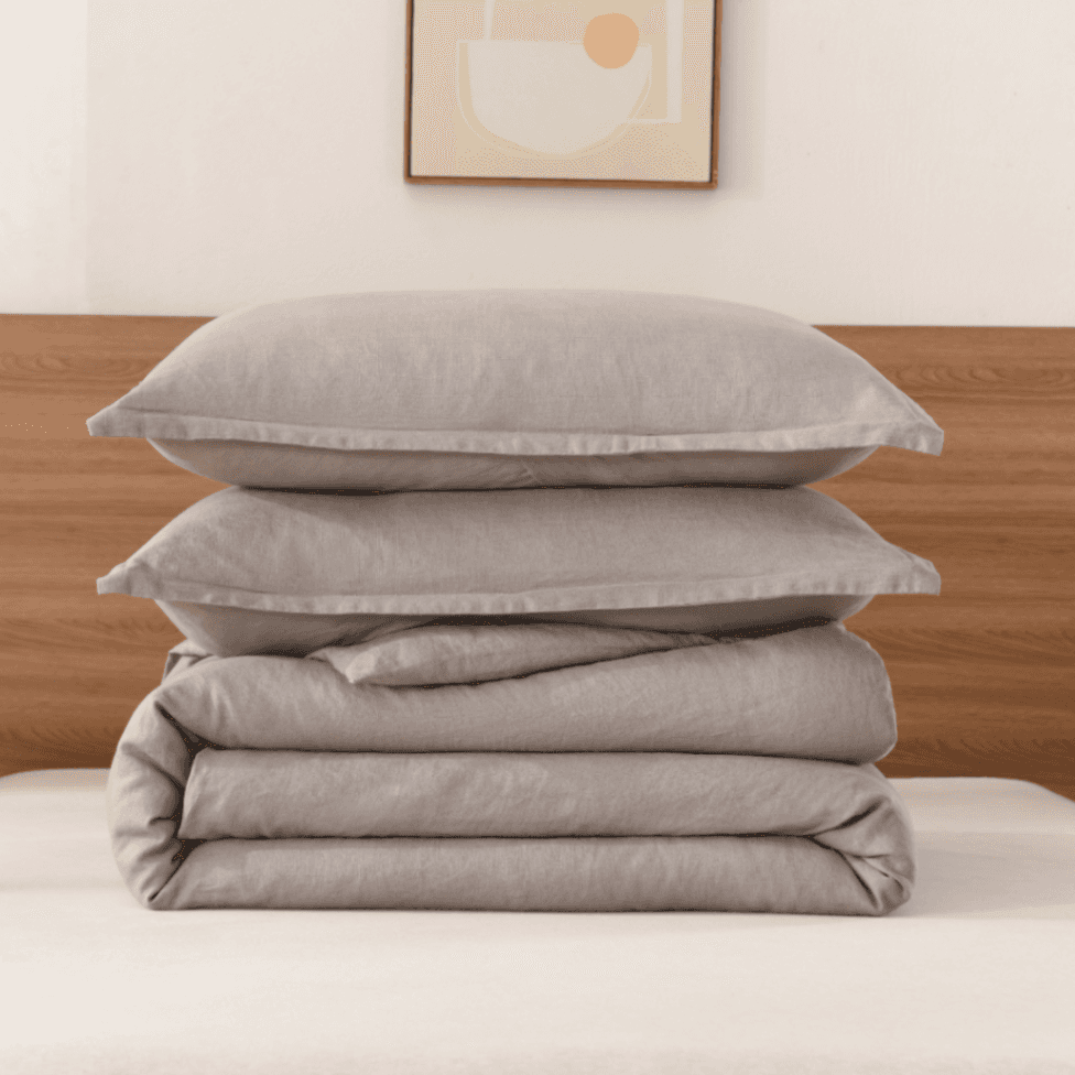 Stack of gray bedding on a bed with a wooden headboard and abstract art in the background.