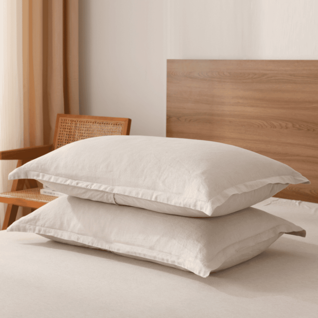 Two beige pillows on a bed with a wooden headboard and chair in the background.