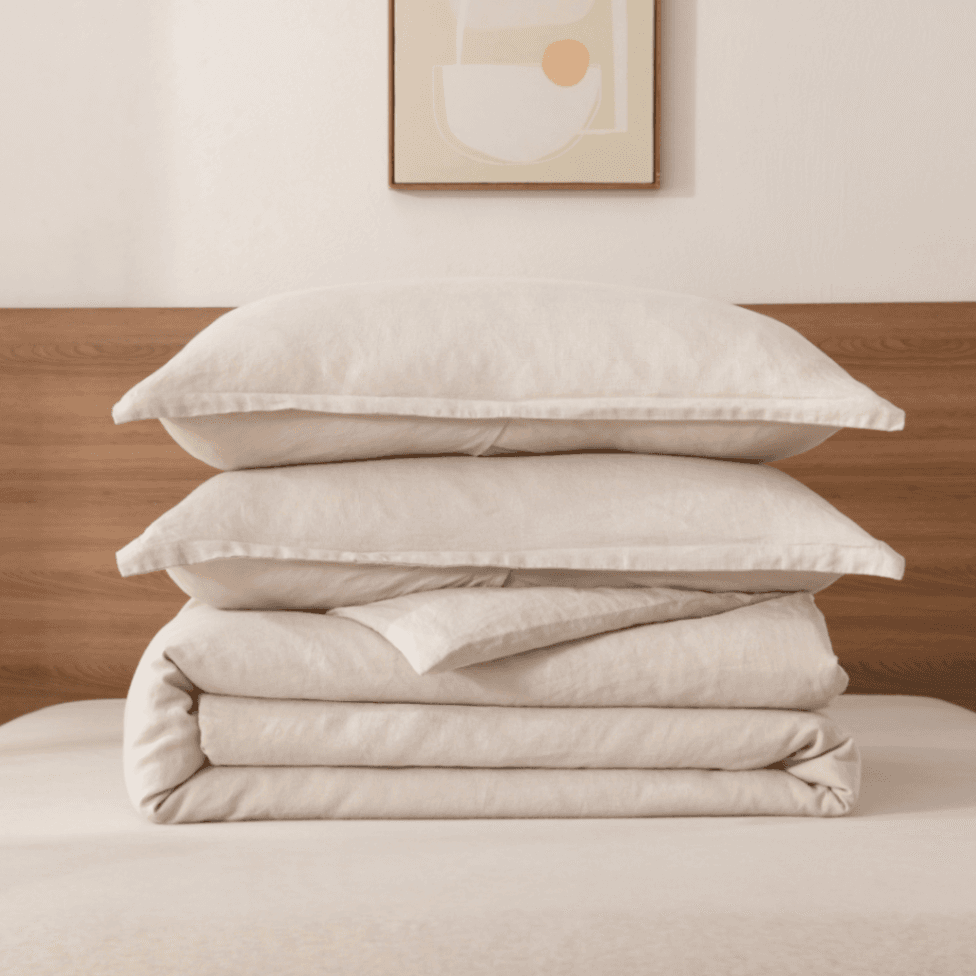 Stack of beige pillows and quilt on a bed with a wooden headboard and abstract art in the background.