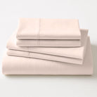 Stack of light pink folded bed sheets on a white background