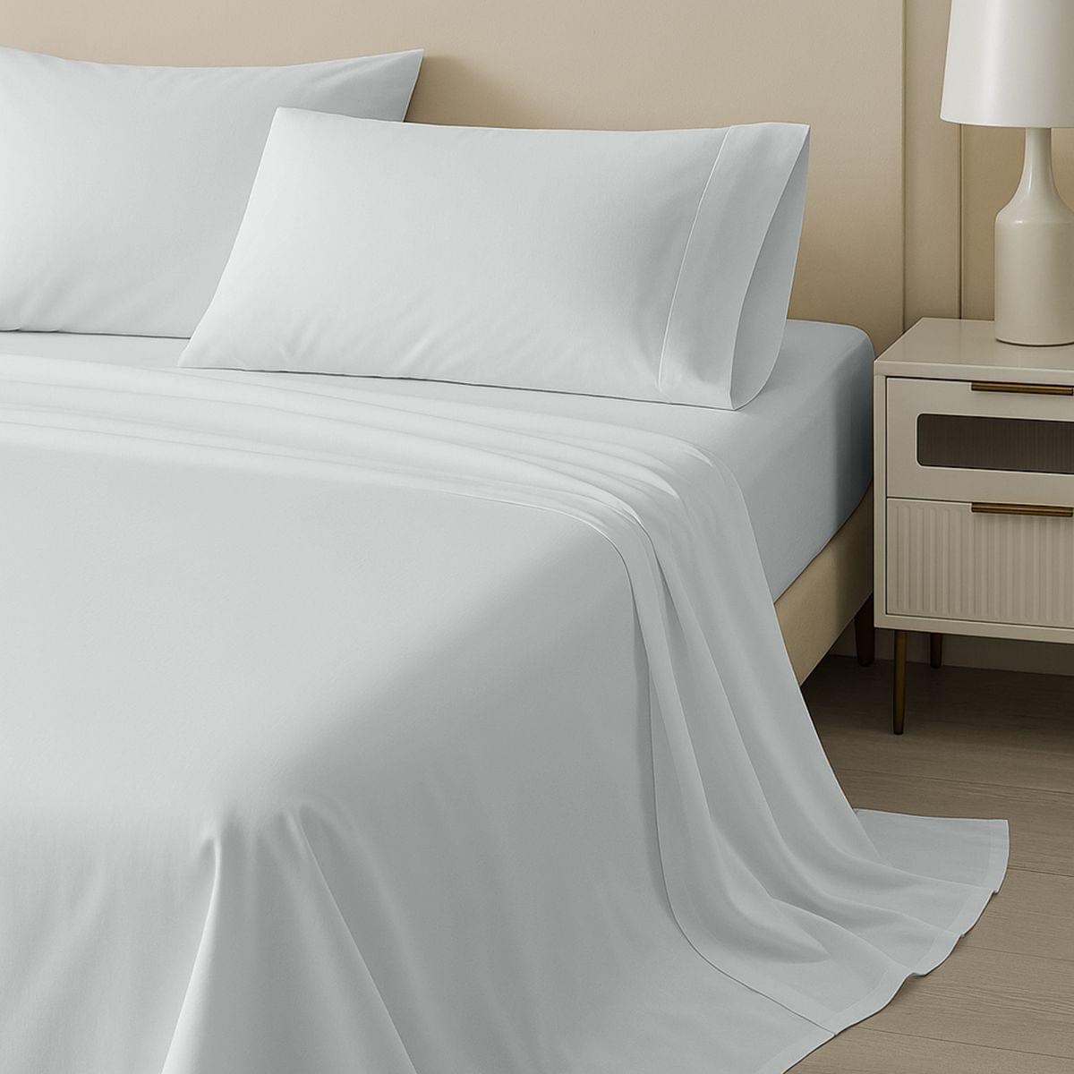 White bed sheets and pillows on a neatly made bed with a nightstand and lamp in the background.