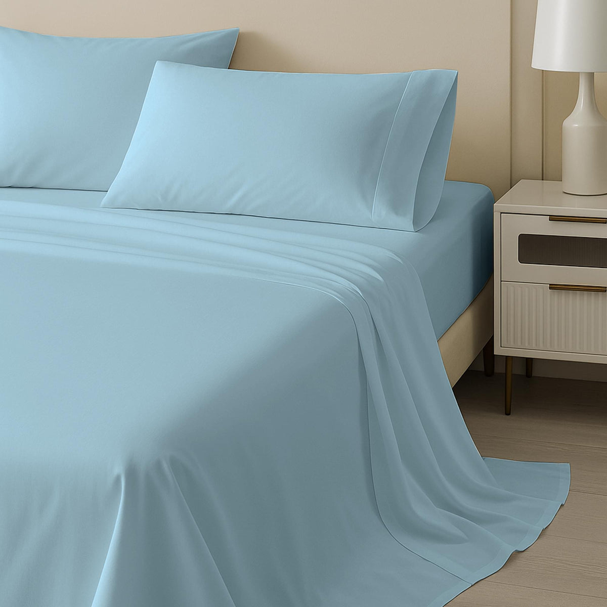 Blue bed sheets and pillows on a bed with a nightstand and lamp in the background.