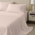 Neatly made bed with light pink bedding and pillows in a bedroom setting.