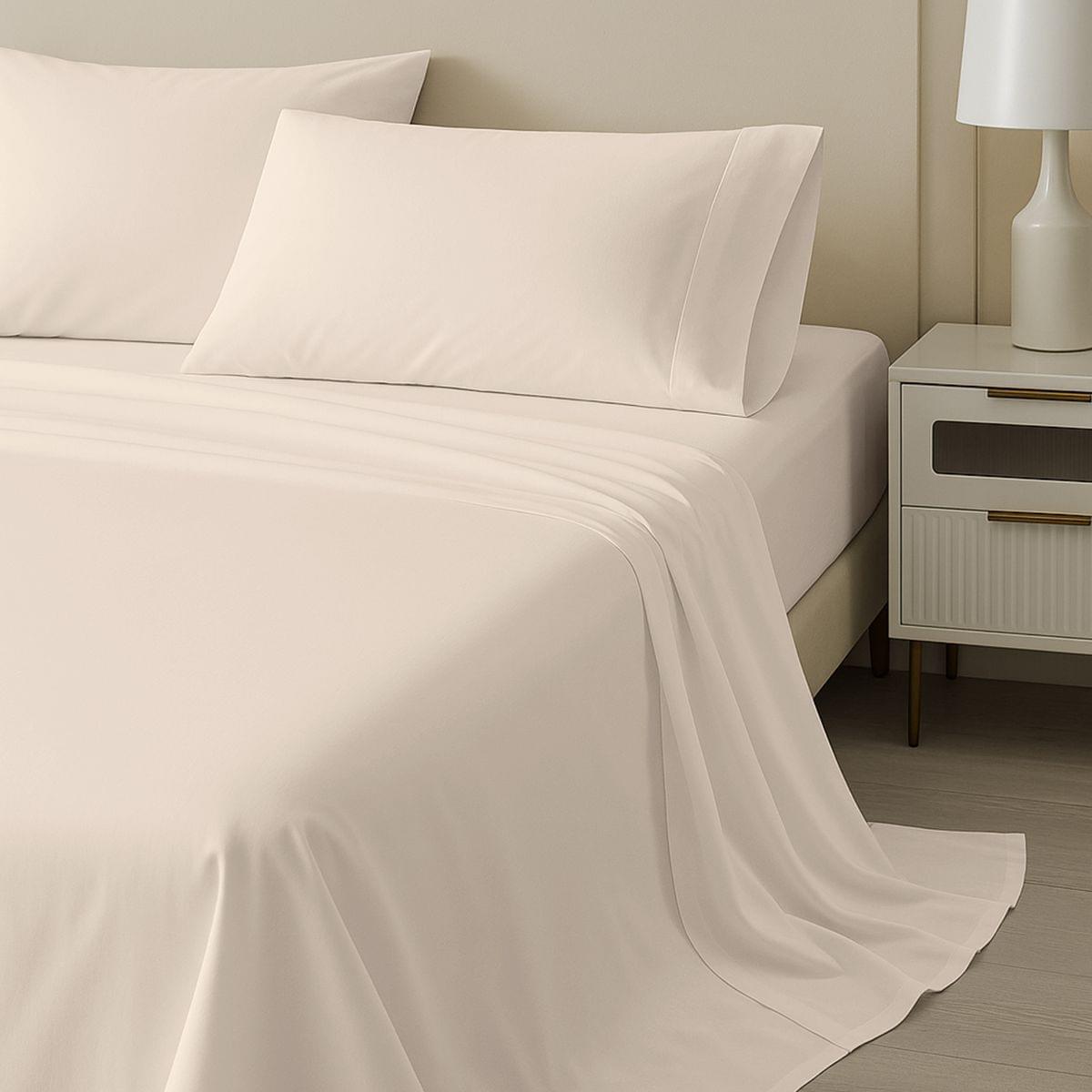 Beige bed 100% Cotton Sheet Set 400 Thread Count and pillows on a bed with a nightstand and lamp in the background.
