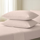 Two beige pillows stacked on a bed with a neutral background
