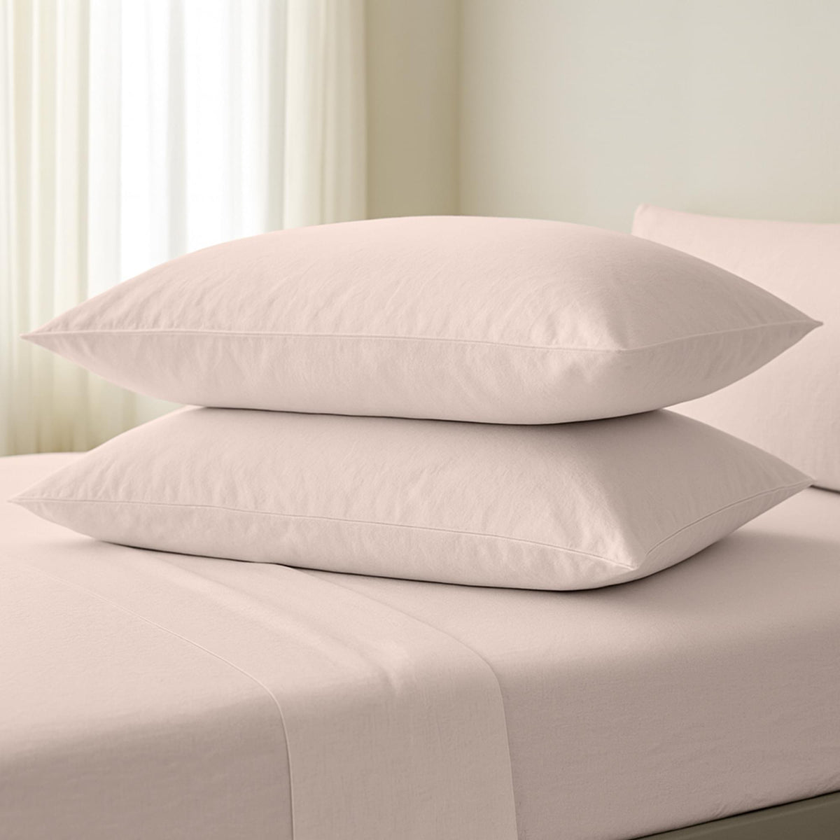 Two beige pillows stacked on a bed with a neutral background