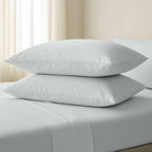 Two white pillows stacked on a bed with light-colored curtains in the background.