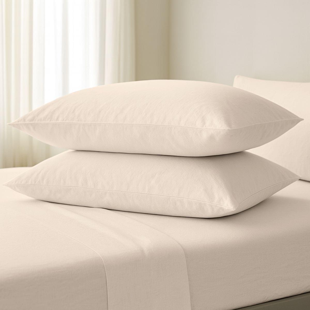 Two beige pillows stacked on a bed with a neutral background