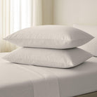 Two white pillows stacked on a bed with a neutral background
