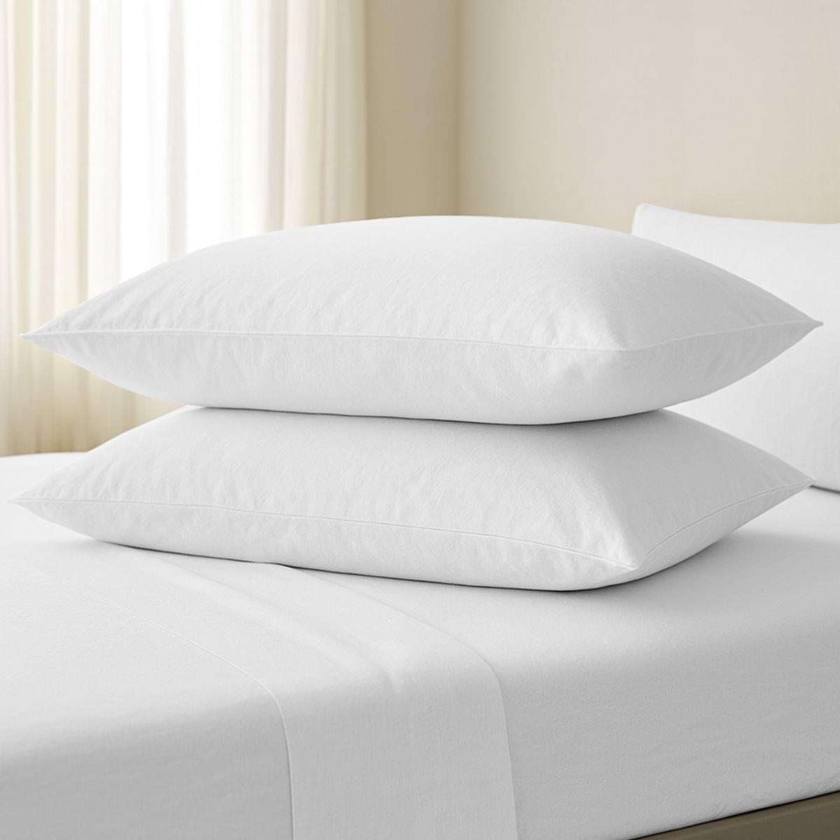 Two white pillows stacked on a bed with a neutral background
