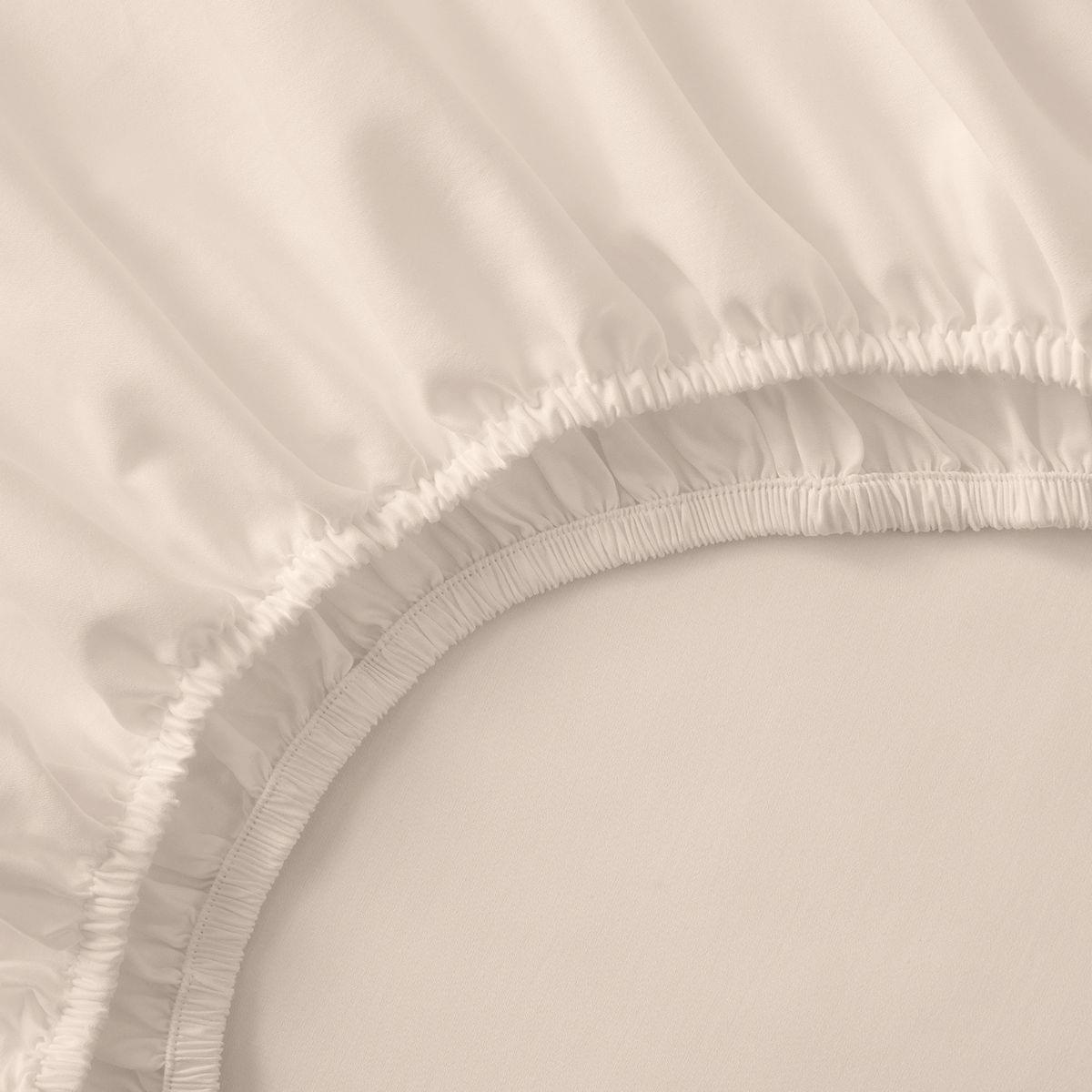 Close-up of a beige fitted sheet with ruffled edge on a bed.