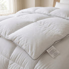 A close-up of a white quilted down Down Alternative Gel Microfiber Duvet with a matching pillow, featuring a small white product tag on the side, set in a softly lit bedroom.