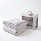 A folded quilted Down Alternative Gel Microfiber Duvet in a light warm gray or off-white tone stands in front of its white branded packaging bag. The packaging shows the text 'NEWCLASON' and 'Gel Hypothermia Queen Protection Layer.