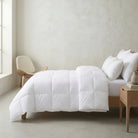 White Down and Feather Duvet on a bed in a minimalistic bedroom with a chair and side table.