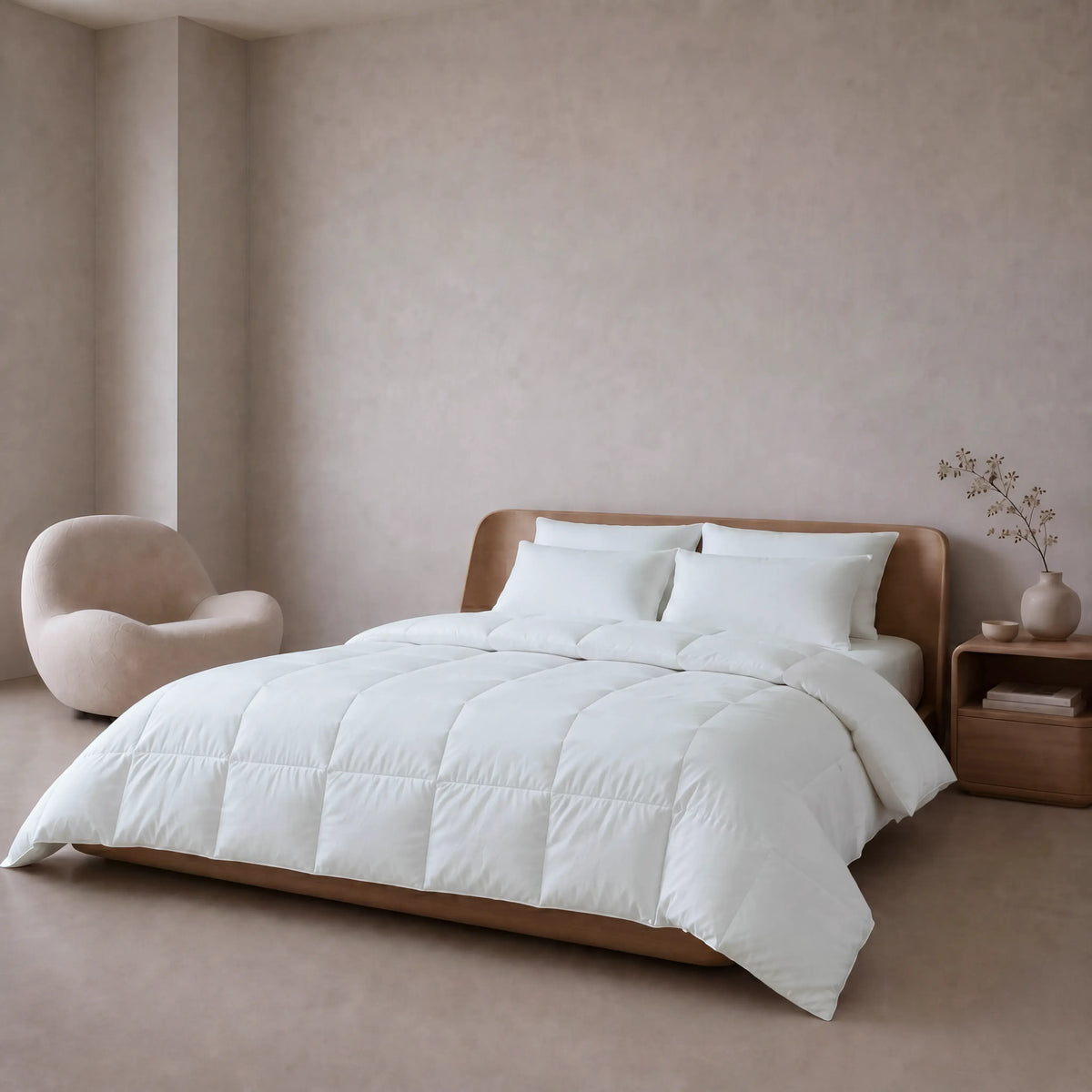 A neatly made bed with a white Down and Feather Products Duvet and two white pillows in a minimalist bedroom with beige walls, a curved chair, and a wooden nightstand.