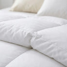 A close-up of a white quilted Down and Feather Products Duvet on a bed, with soft white pillows visible in the background.