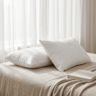 Two white Down and Feather Pillow on a beige bed with a light background