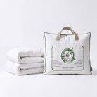 A folded white All Season Bamboo Duvet White Insert next to its white storage bag with green trim and tan handles. The bag features a large front label with the brand name 'zen dream' and product details, set against a clean white background.