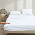 Person adjusting a fitted Organic Cotton Sheet Set 500 Thread Count on a bed in a minimalistic room.
