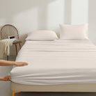 Person adjusting a fitted Organic Cotton Sheet Set 500 Thread Counton a bed in a minimalistic room.