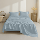 Light blue bedding set on a bed in a room with a chair and side table.