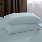 Light blue bed sheets and pillows on a bed with a neutral background