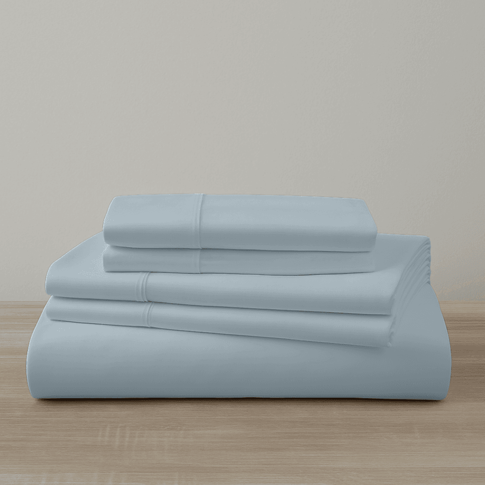 Set of light blue bed sheets and pillowcases on a wooden surface with a neutral background