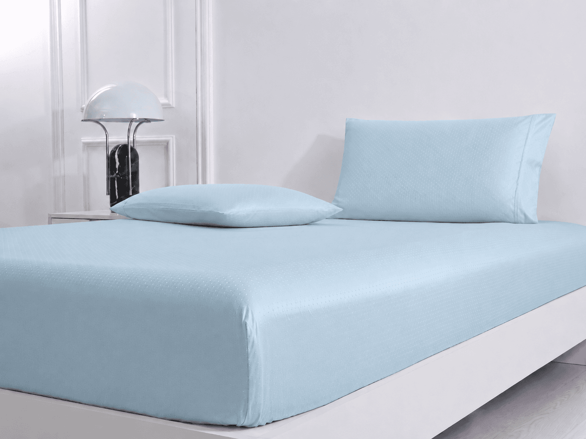 Light blue 600 Thread Count Jacquard Swiss Dot 100% Cotton Sheet Set on a bed with a white nightstand and lamp in the background.