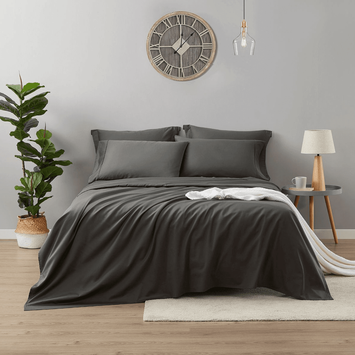Gray bedding set on a bed in a bedroom with a clock and plant.