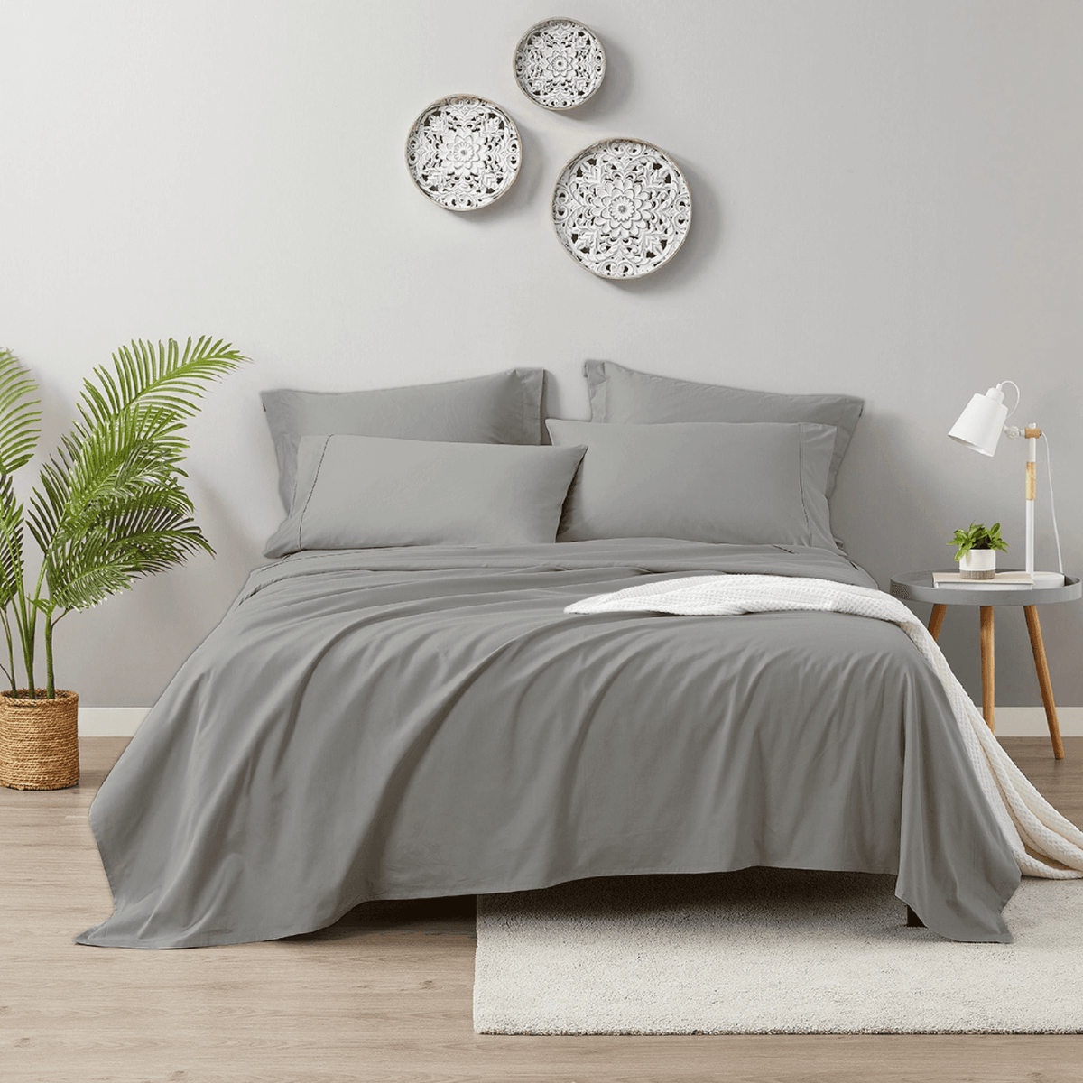 Gray bedding set on a bed in a bedroom with decorative plates on the wall.