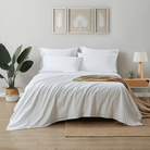 Neatly made bed with white bedding and a beige blanket in a bedroom setting.